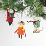 Three felt mouse ornaments dressed for winter—one in a red coat and plaid hat tossing a snowball, one in an orange coat with a yellow scarf holding a snowball, and one in a green sweater holding red berries—shown hanging on a tree
