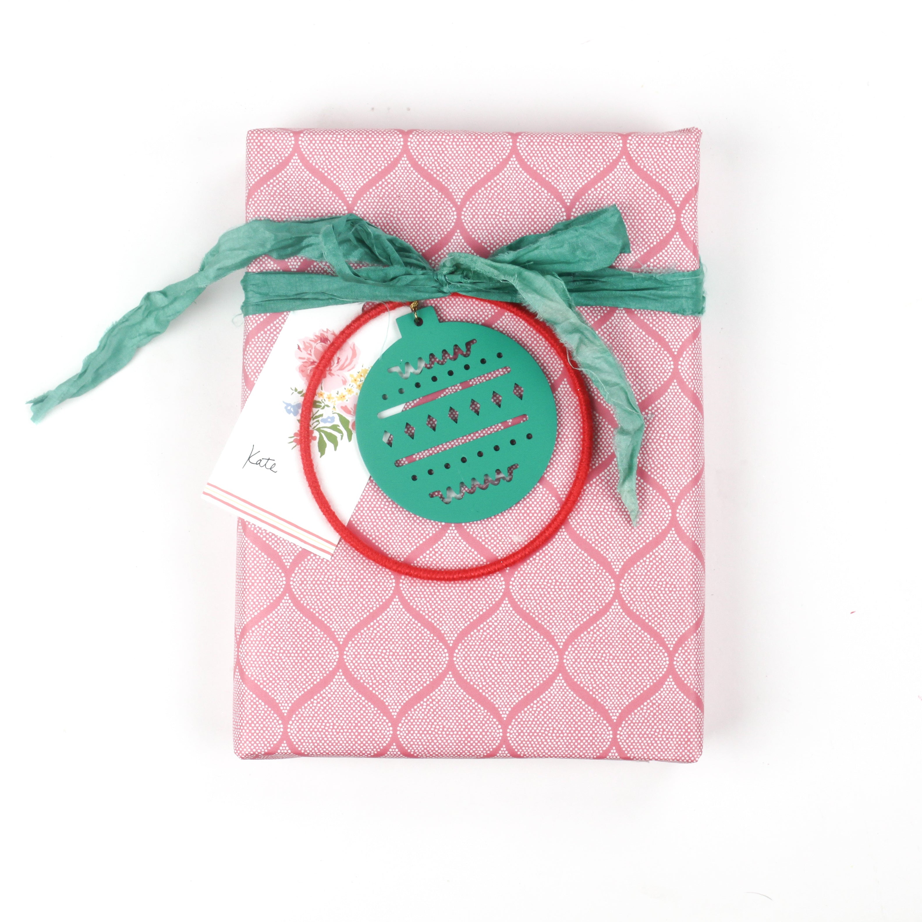 Gift wrapped in pink lattice pattern paper with green ribbon and holiday ornament tag.