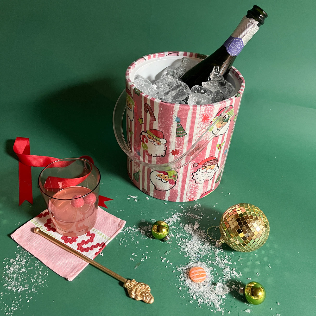 pink and white filled ice bucket surrounded by a cocktail, candies and ornaments.