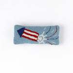 Rectangular blue decorative pillow with a hooked texture featuring a red, white, and blue fireworks rocket design, shown on a white background.