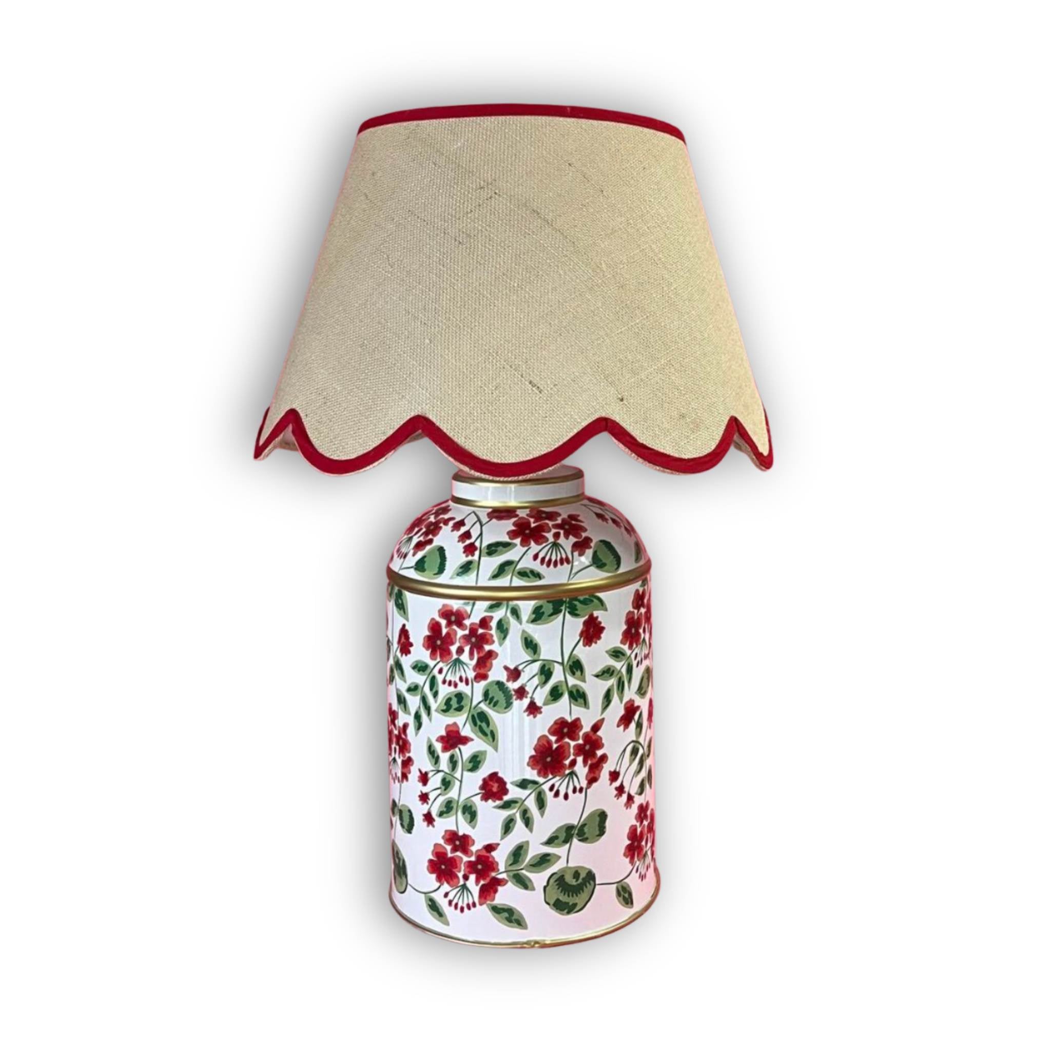 White ginger jar table lamp decorated with red and green floral patterns, paired with a beige scalloped linen lampshade trimmed in red.