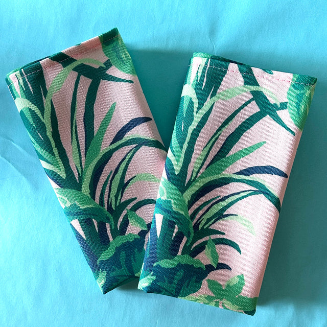 A pair of folded napkins in Jungle Road print in greens and pink on a turquoise background.