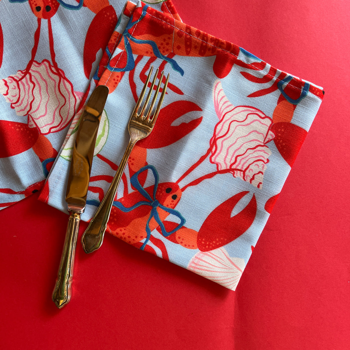 Folded Rock Lobster cloth dinner napkin with cutlery on a red background.