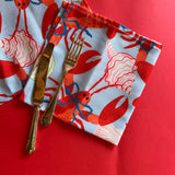 Folded Rock Lobster cloth dinner napkin with cutlery on a red background.
