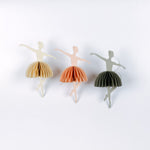 Three paper ballerina christmas ornaments in different colors on a white background