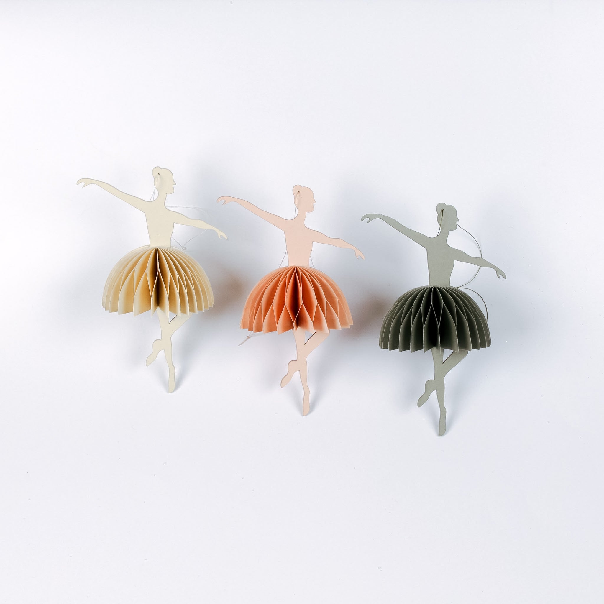 Three paper ballerina christmas ornaments in different colors on a white background