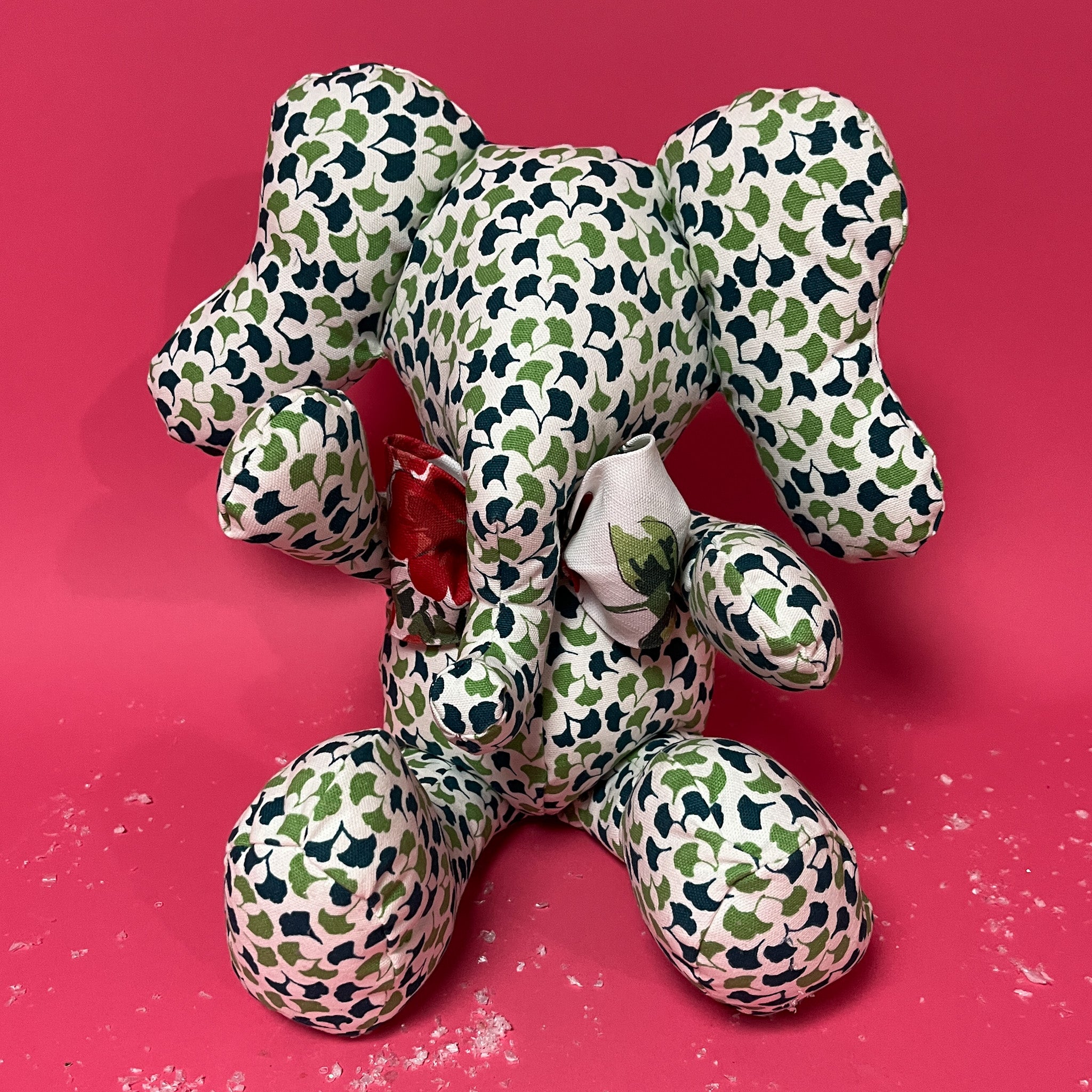 Green and white patterned stuffed elephant toy with a red bow in a red background.