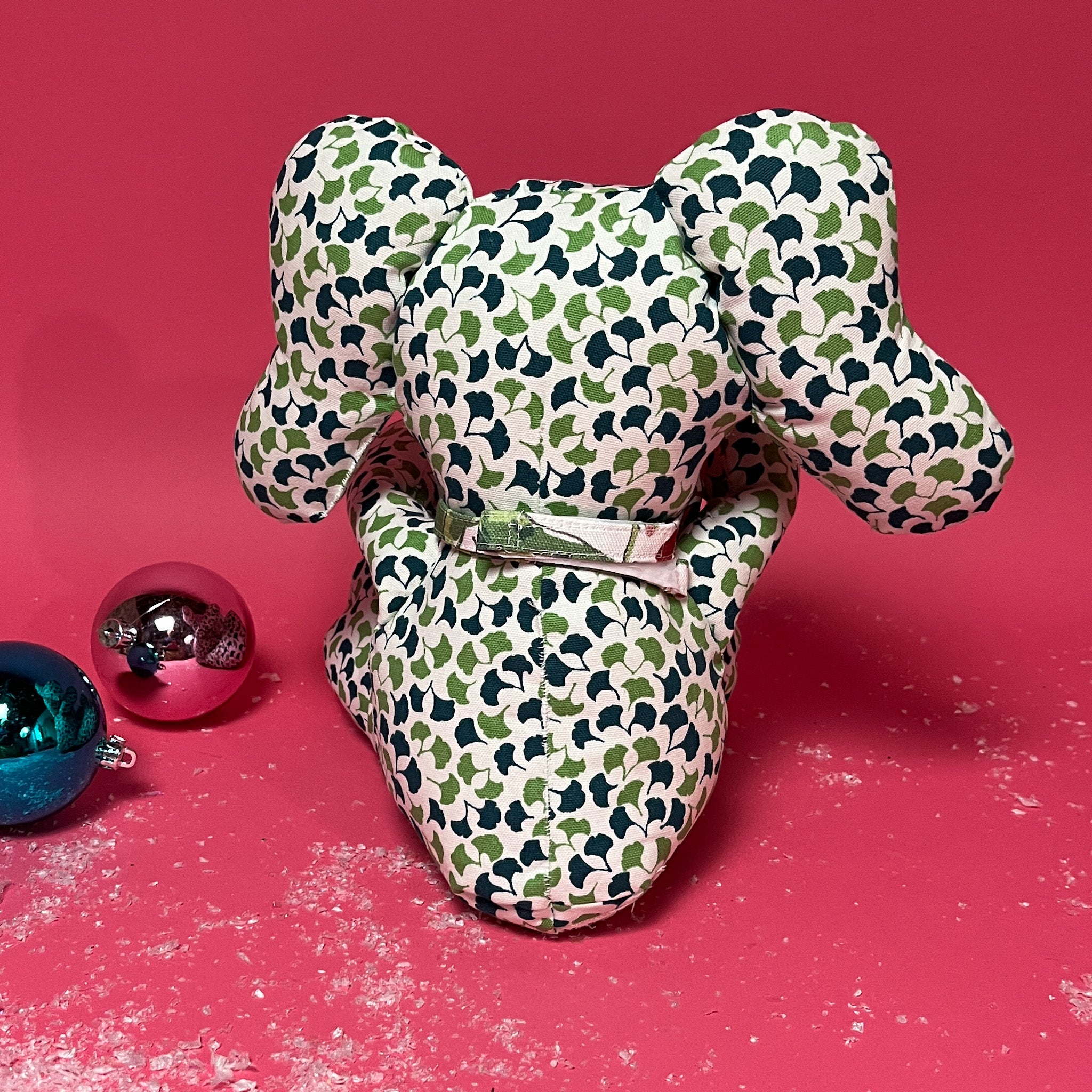 Green and white patterned stuffed elephant toy with a red bow back in red background.
