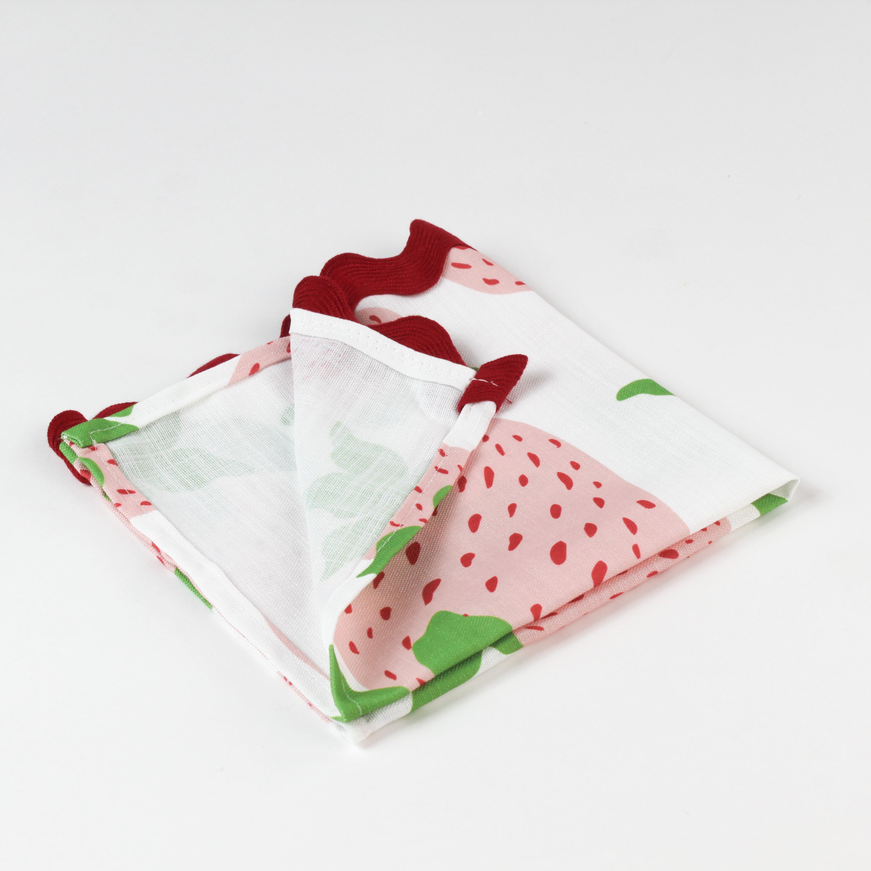 Close-up of folded cloth napkin featuring a strawberry print with red scalloped trim.