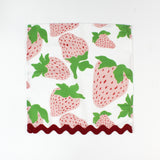 Cloth napkin laid flat with a large pink strawberry print and red scalloped trim.