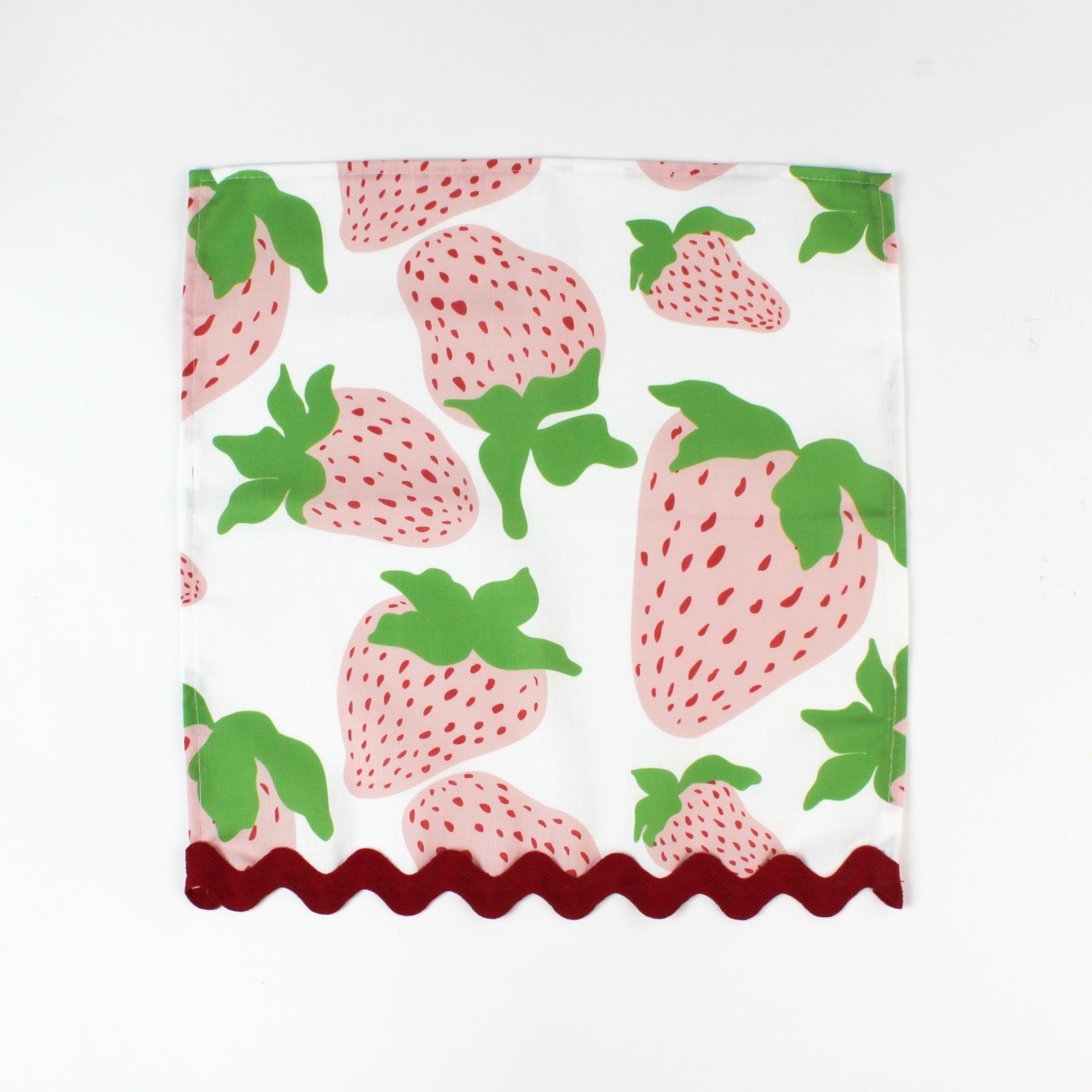 Cloth napkin laid flat with a large pink strawberry print and red scalloped trim.