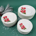 Three white dinner plates with red poinsettia floral design arranged on a green background with snow-like accents.