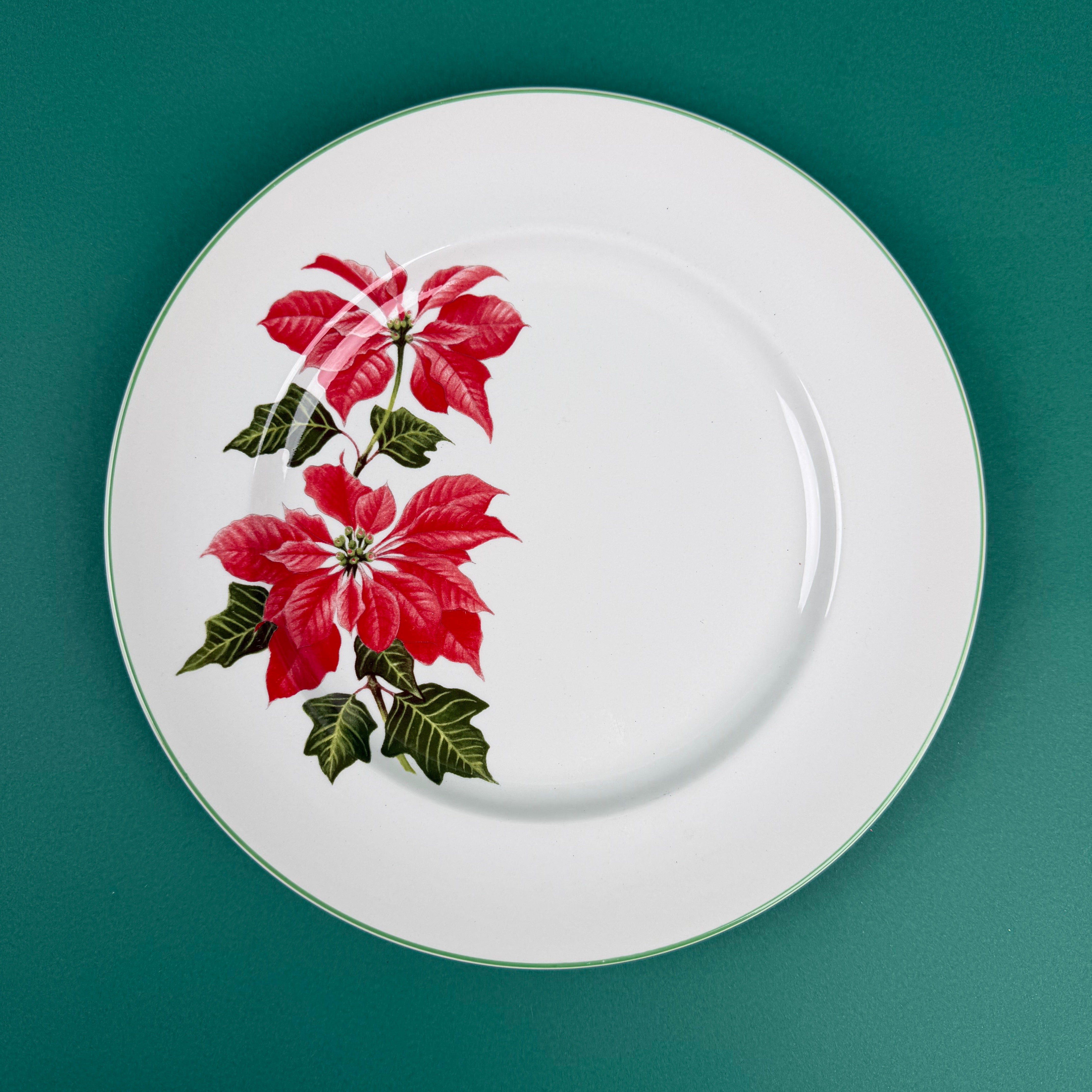 White dinner plate with a red poinsettia floral design on the left side, displayed on a green background.