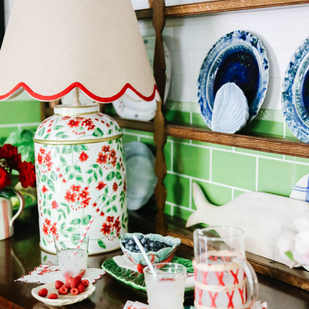 a red white and green lamp with a floral motif surrounded by bowls with berries and a pitcher and glass
