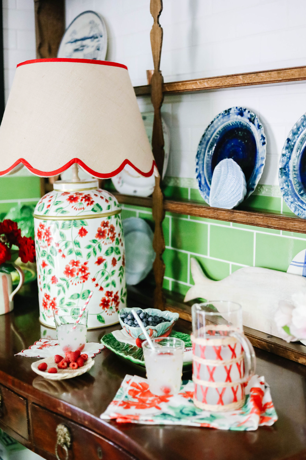 a red white and green lamp with a floral motif surrounded by bowls with berries and a pitcher and glass