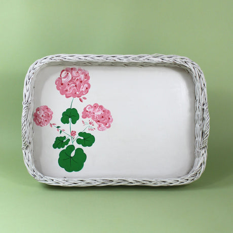 A vintage wicker tray with a painted geranium motif on the tray base. 