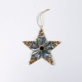 Gilt metal star shaped Christmas ornament decorated with blue and iridescent crystal accents and a dark gemstone at the center, displayed against a white background.