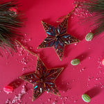 Two gilt metal star shaped Christmas ornaments decorated with colorful crystal accents