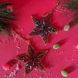 Two gilt metal star shaped Christmas ornaments decorated with colorful crystal accents