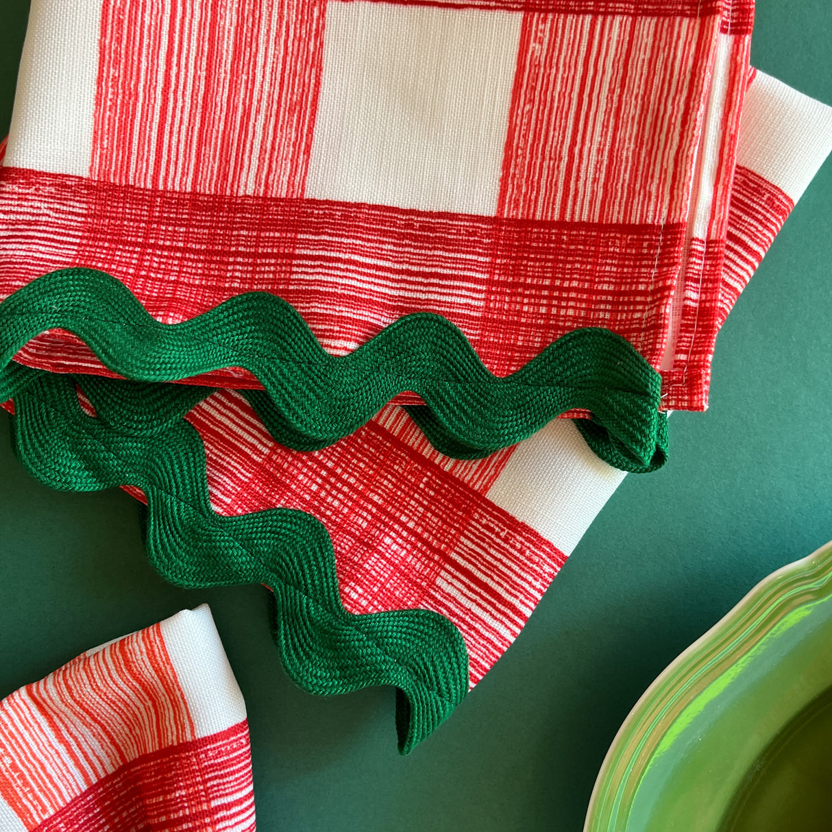 Close-up view of Gin Lane Geranium Red gingham cloth dinner napkins with green ric rac trim.