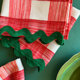 Close-up view of Gin Lane Geranium Red gingham cloth dinner napkins with green ric rac trim.