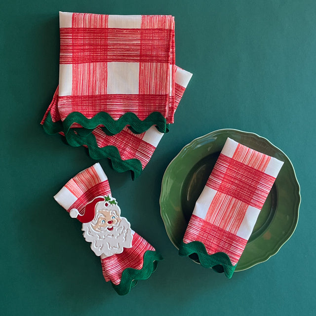 Gin Lane Geranium Red w/ green Ric Rac cloth Dinner Napkins shown on a green plate and one gathered into a Santa napkin ring.