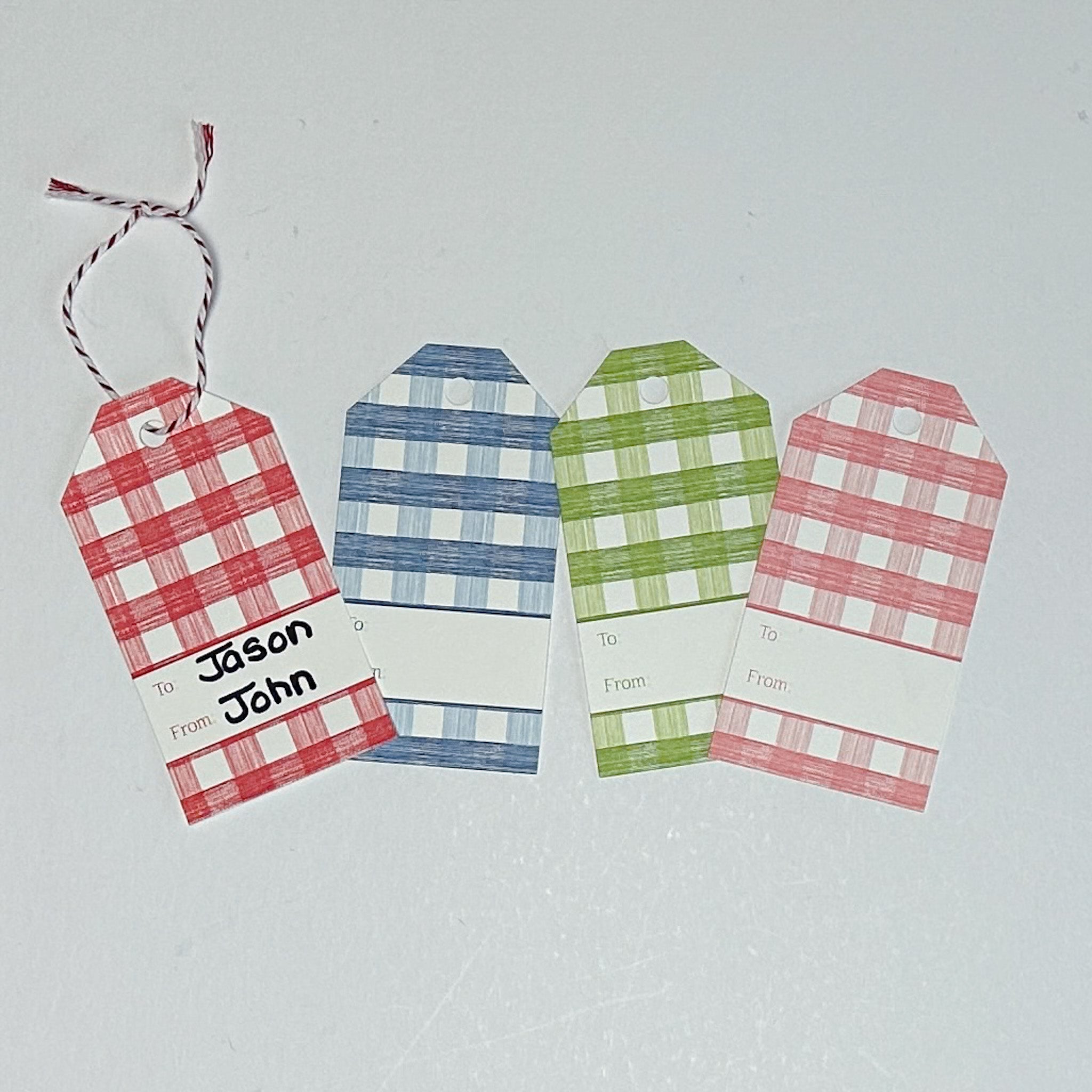 A set of three gingham patterned gift tags in red, blue, and green with a white space for personalization on the back, displayed on a white background.