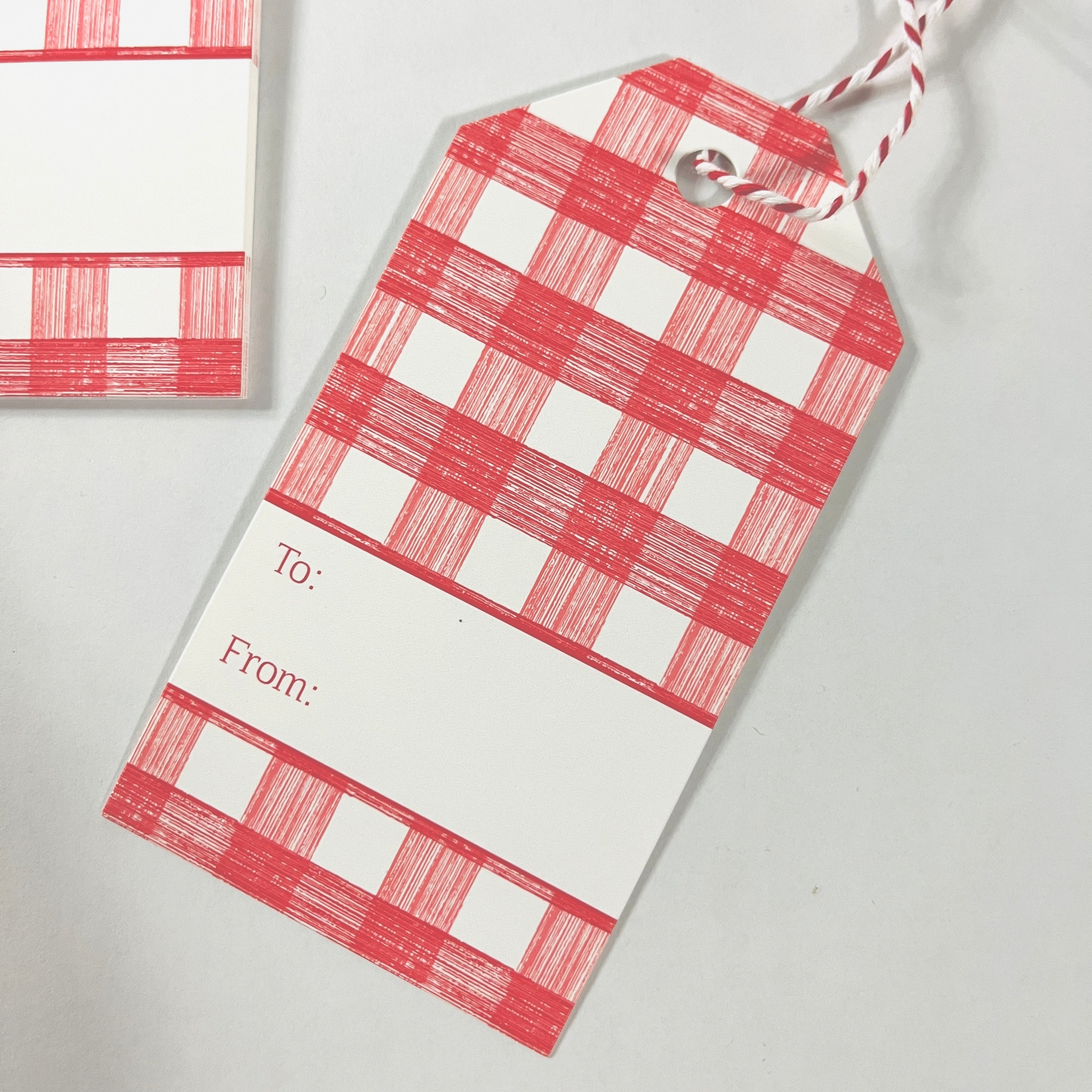 A red gingham patterned gift tags with a white space for personalization on the back, displayed on a white background.