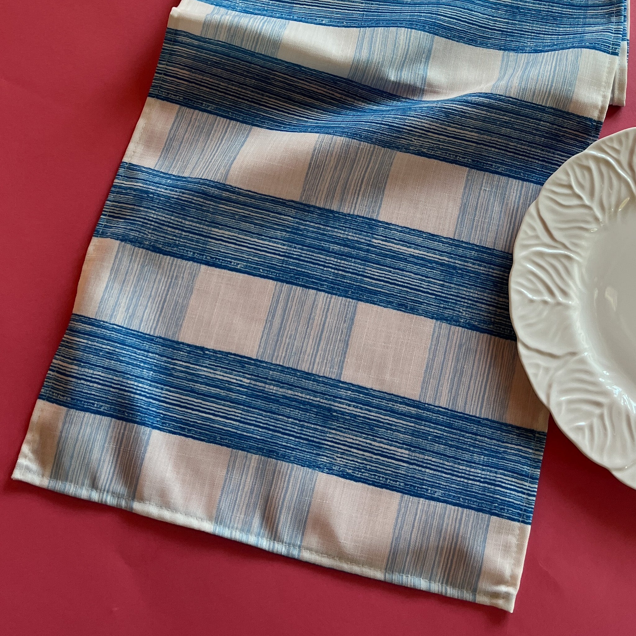 The Gin Lane cloth table runner is a gingham print in Swedish Blue shown on a red background