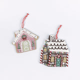 Two gingerbread house Christmas ornaments, one pink and one brown with candy cane details, shown with red and white hanging strings in white background