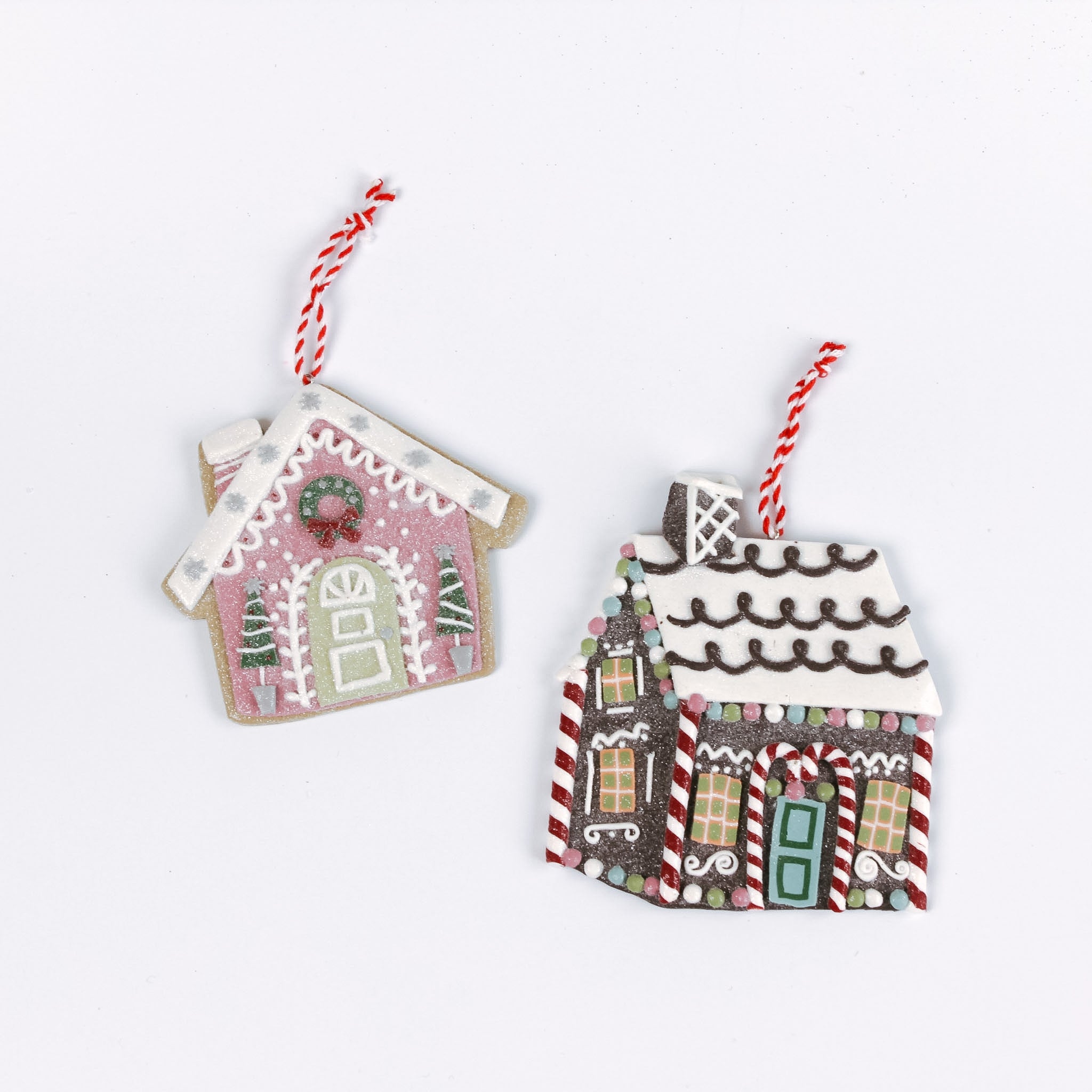 Two gingerbread house Christmas ornaments, one pink and one brown with candy cane details, shown with red and white hanging strings in white background