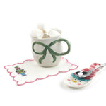 Mug with green bow, marshmallows, and a decorative spoon on a white background