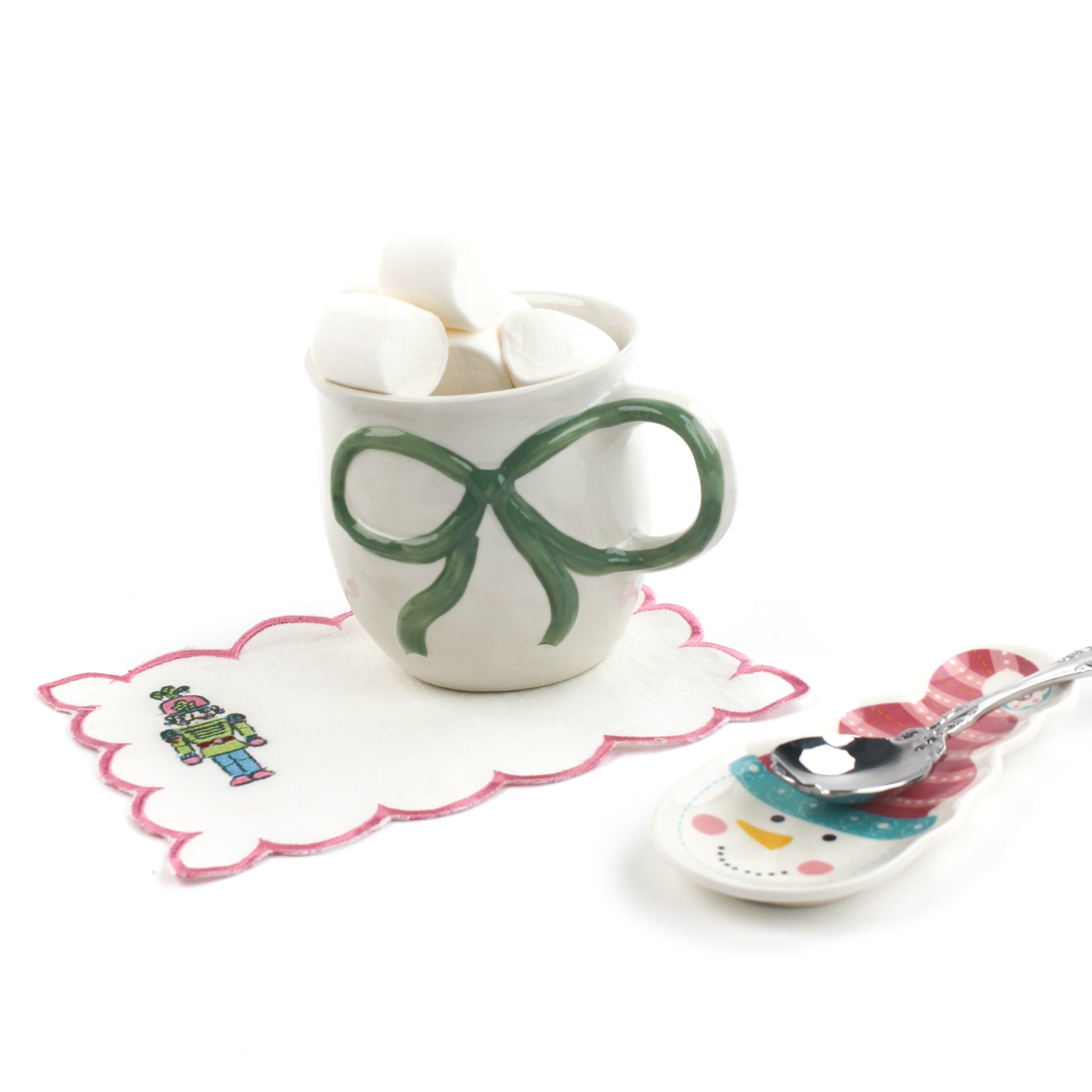 Mug with green bow, marshmallows, and a decorative spoon on a white background