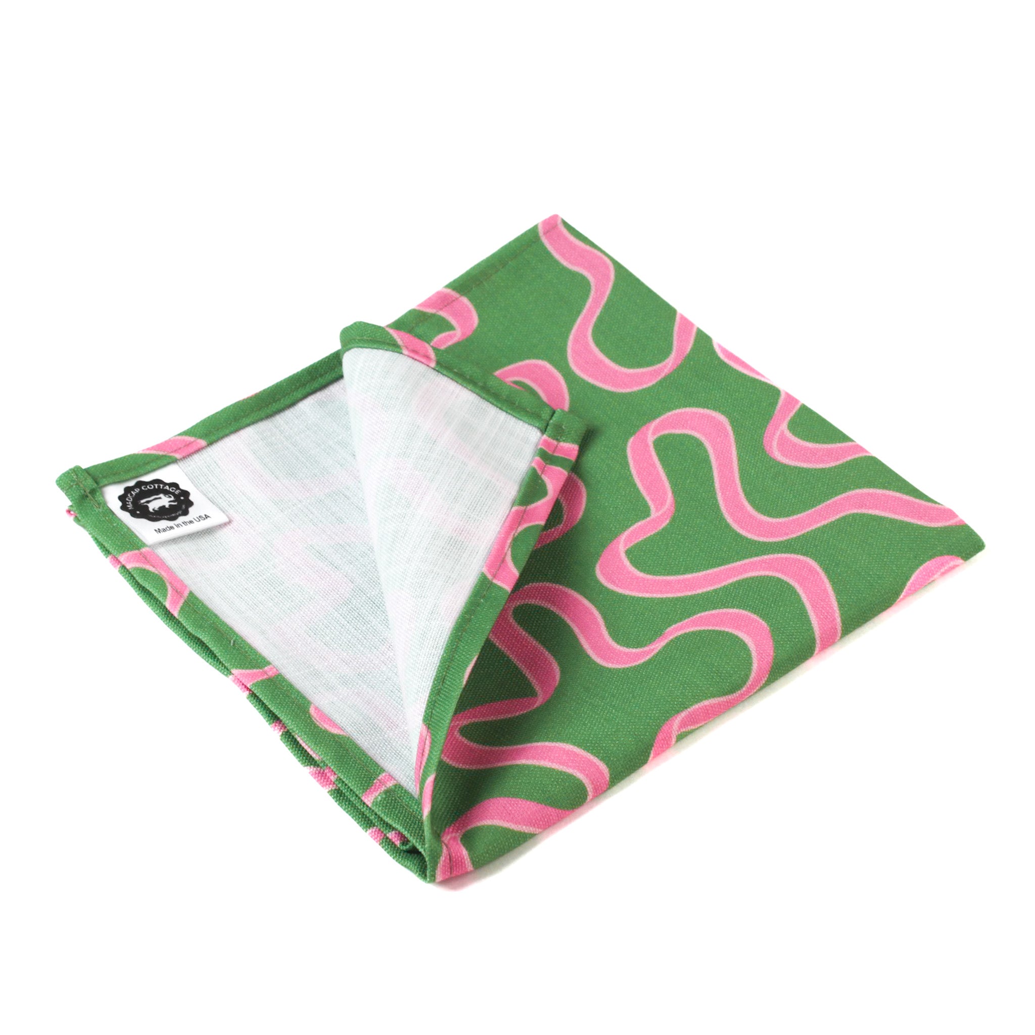 Green napkin with playful pink squiggle pattern and stitched edges on a white background, modern table linen perfect for Christmas tea towel styling, holiday entertaining, and seasonal home décor