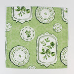 Green fabric napkin with a vintage plate and botanical print laid flat.