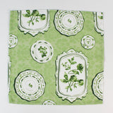 Green fabric napkin with a vintage plate and botanical print laid flat.