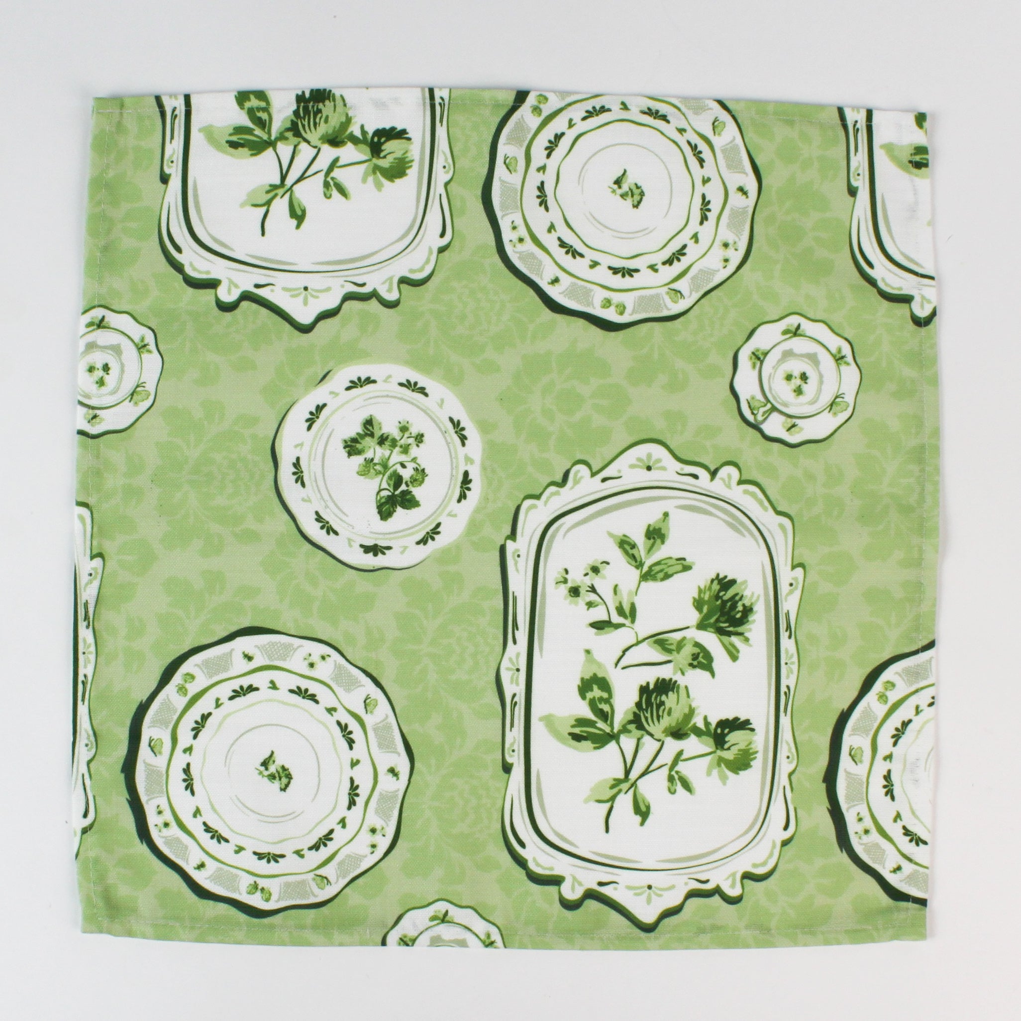 Green fabric napkin with a vintage plate and botanical print laid flat.
