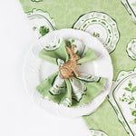 Green vintage-style patterned napkin displayed on a white plate with a gold rabbit napkin ring.