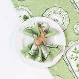 Green vintage-style patterned napkin displayed on a white plate with a gold rabbit napkin ring.