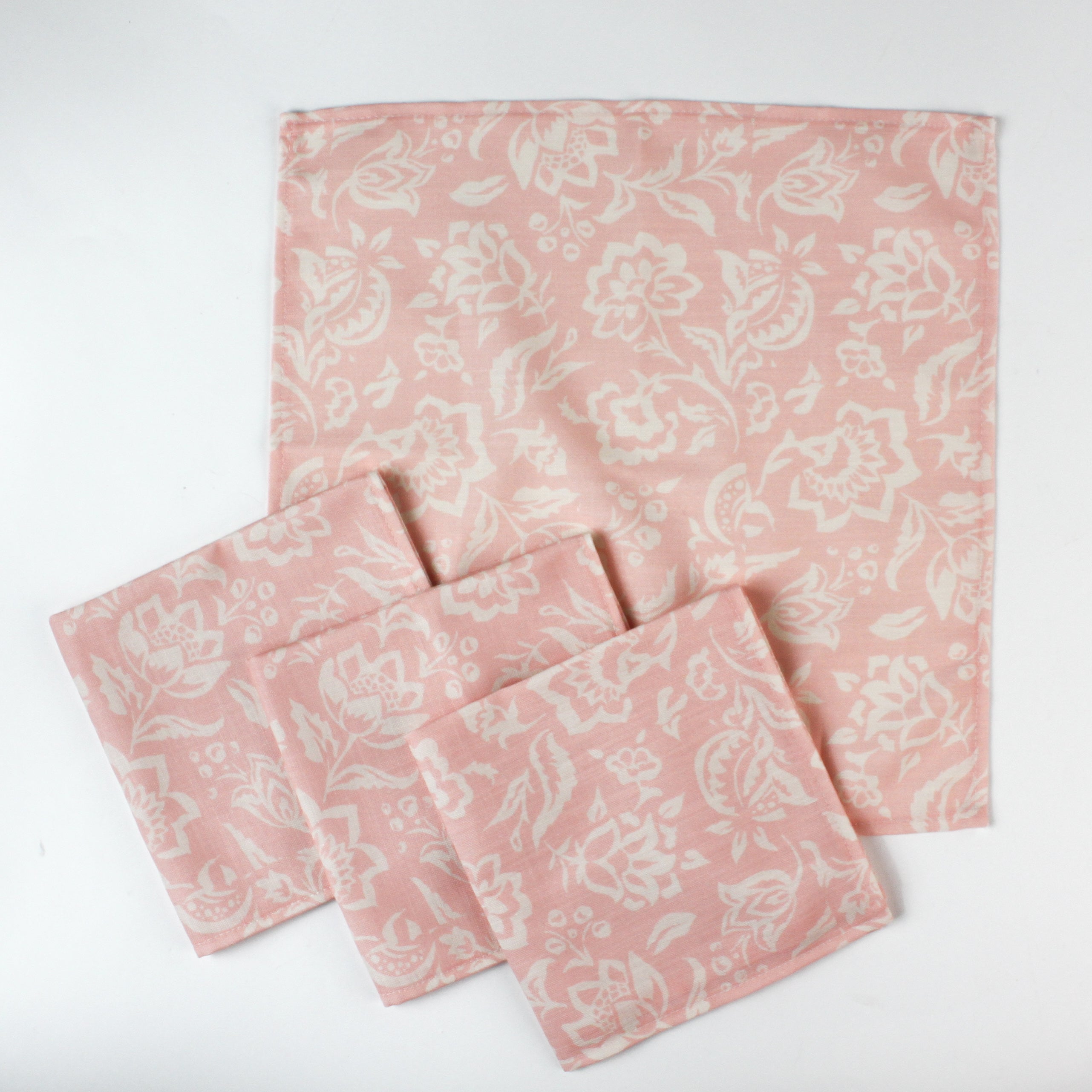 Set of four pink floral cotton cloth napkins displayed with one full napkin and three folded pieces on a white background.
