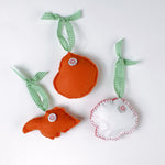 back of Handcrafted Pink Orange Shells Felt Christmas Ornaments featuring coral spiral, conch, and red scallop shell designs with green gingham ribbons.