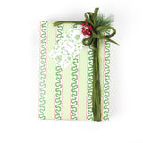 Green patterned Christmas gift box wrapped in holiday paper with decorative green ribbon and berry embellishment, shown from a top-down view.