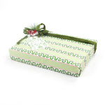 Green patterned Christmas gift box wrapped in light green paper with holly-inspired stripes and topped with a green ribbon and festive berry decoration.