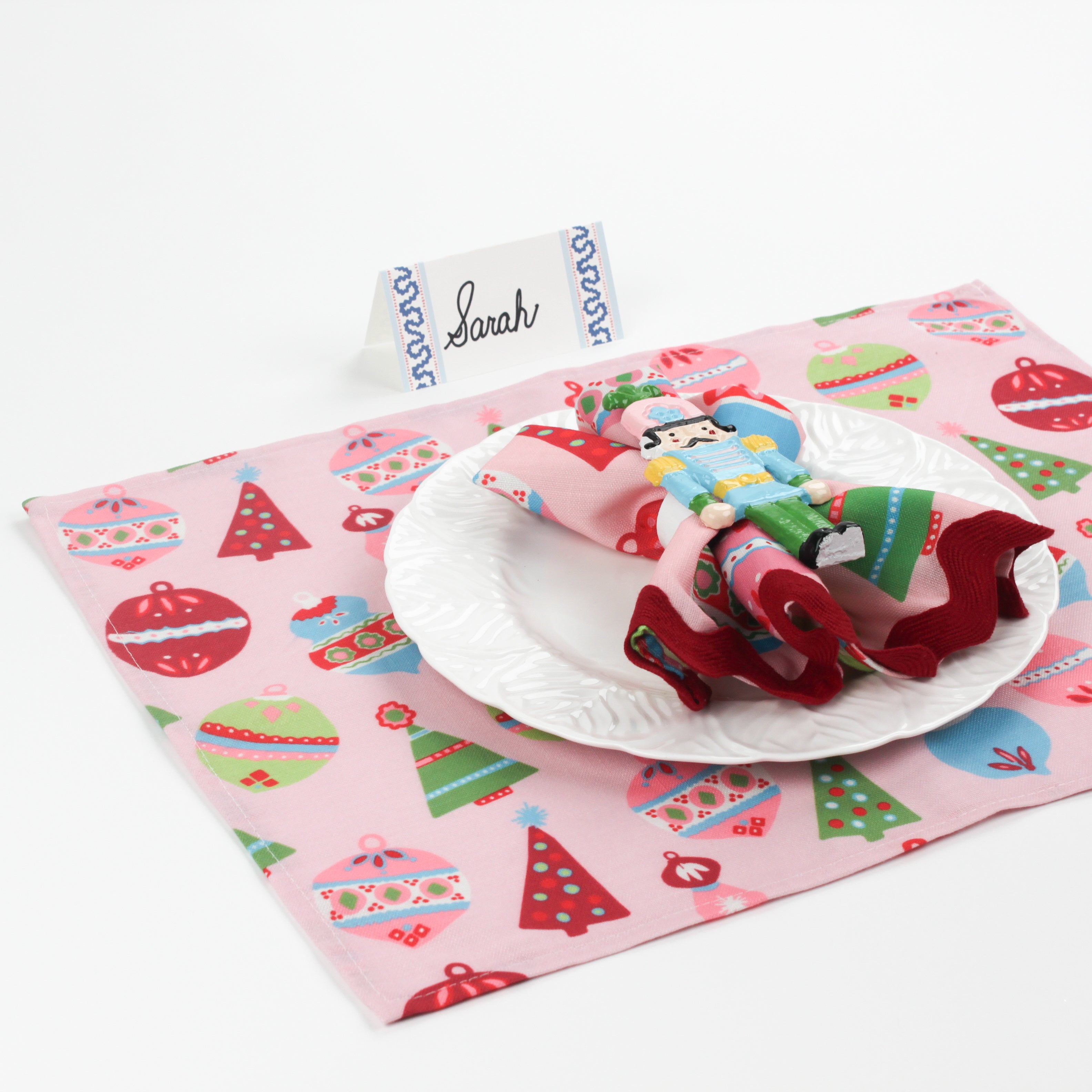 Side angle view of Harbor Trail Paper Place Card in blue displayed on a Christmas-themed table with pink placemat, nutcracker napkin, and white dinner plate.