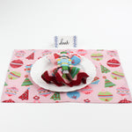 Christmas table setup featuring Harbor Trail Paper Place Card in blue with pink holiday placemat, nutcracker napkin ring, and white plate for festive dining decor.