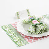 table setup featuring Harbor Trail Paper Place Card in green with pink and green holiday placemat, white plate, and decorative napkin ring.