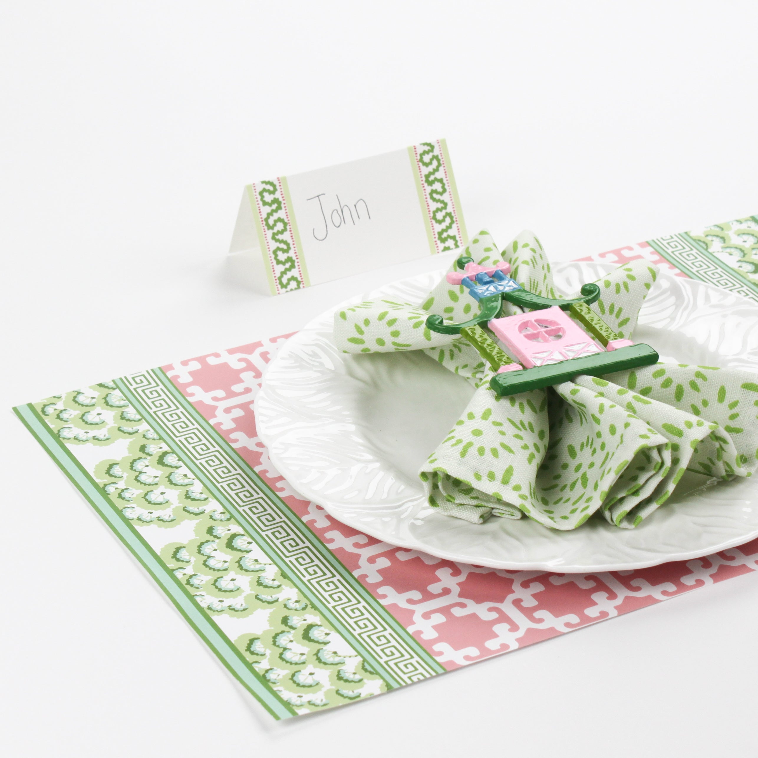 table setup featuring Harbor Trail Paper Place Card in green with pink and green holiday placemat, white plate, and decorative napkin ring.