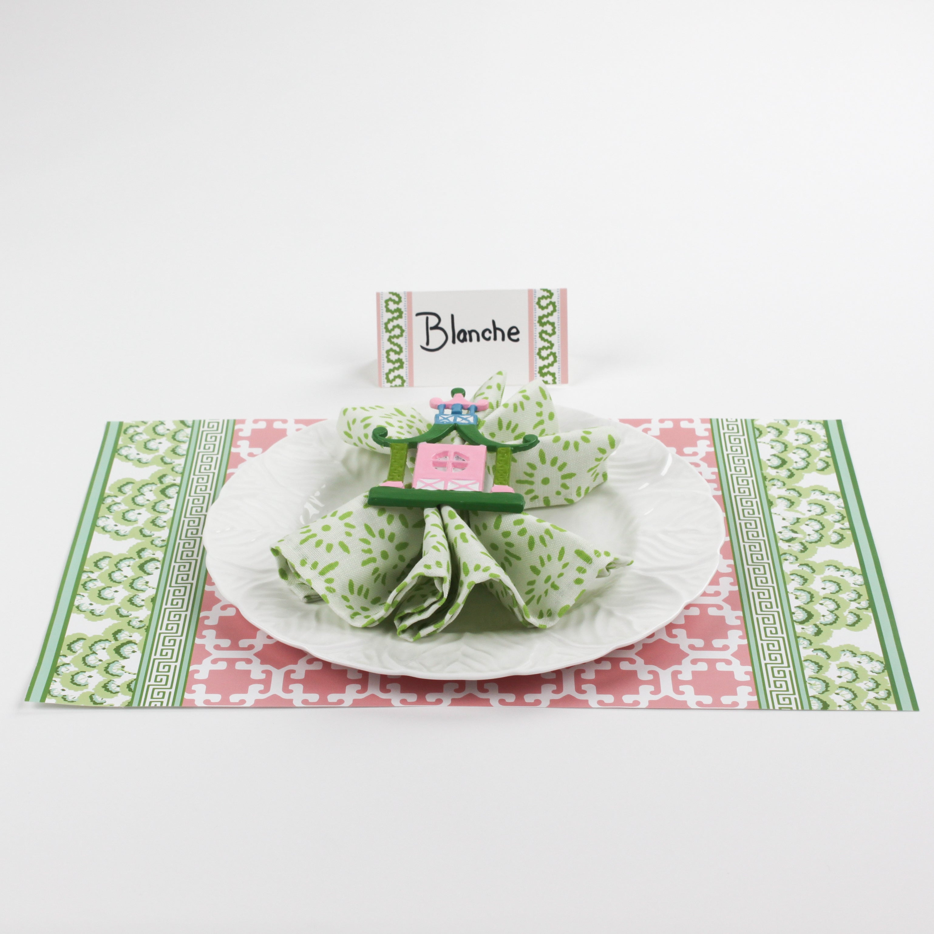 Christmas table setup featuring Harbor Trail Paper Place Card in green and pink, white plate, floral napkin, and festive holiday placemat.