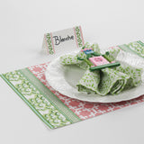 Side view of Harbor Trail Paper Place Card in green and pink on a Christmas table with patterned green and pink placemat and white dinnerware.