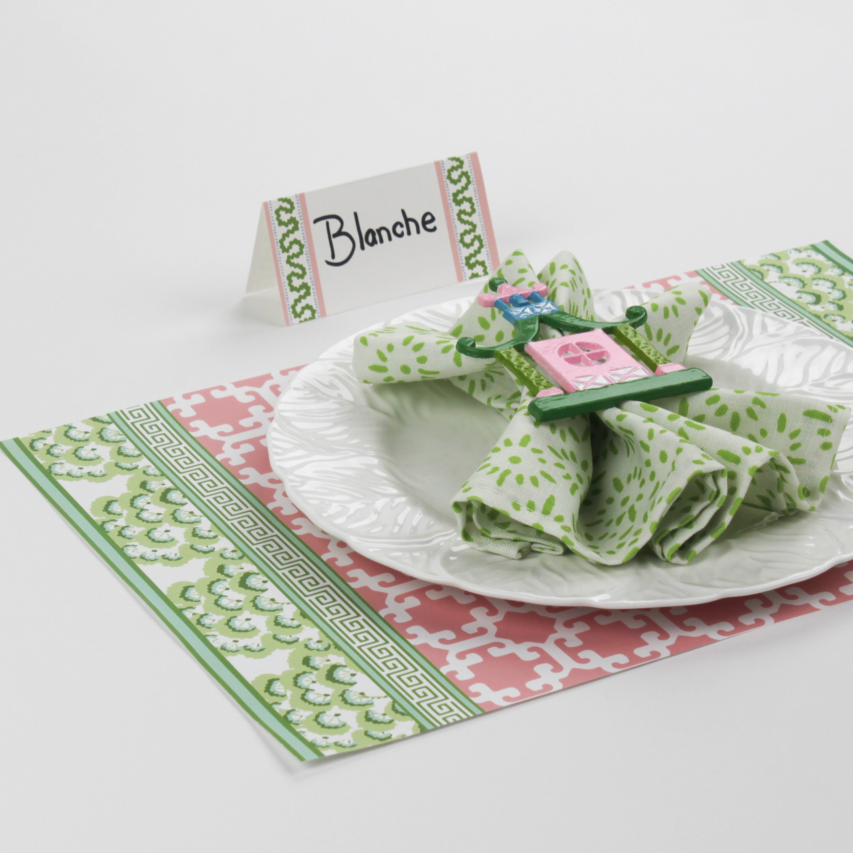 Side view of Harbor Trail Paper Place Card in green and pink on a Christmas table with patterned green and pink placemat and white dinnerware.